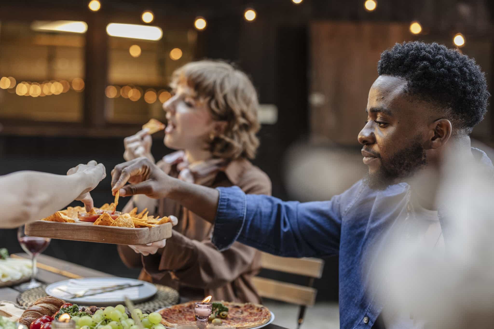 Friends eating nachos and pizza at a multiracial party outdoors
